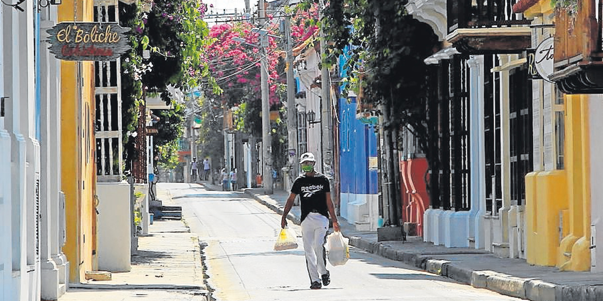 Un hombre carga bolsas con víveres mientras camina por una desolada calle durante la ‘cuarentena’ nacional, en Cartagena, ciudad que ayer reportó la muerte de una mujer.